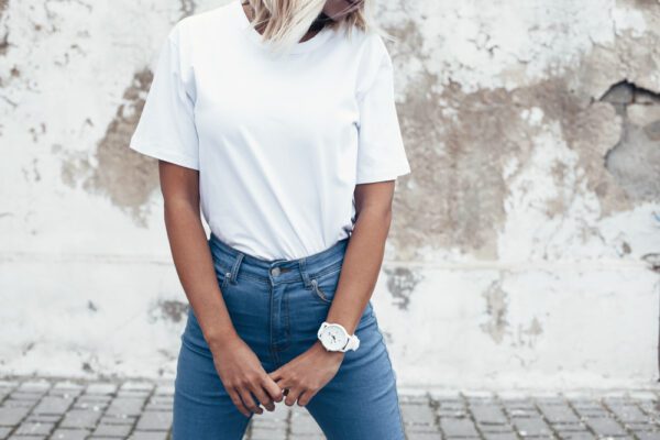 Hipster girl wearing blank white t-shirt and jeans posing against rough street wall, minimalist urban clothing style, mockup for tshirt print store