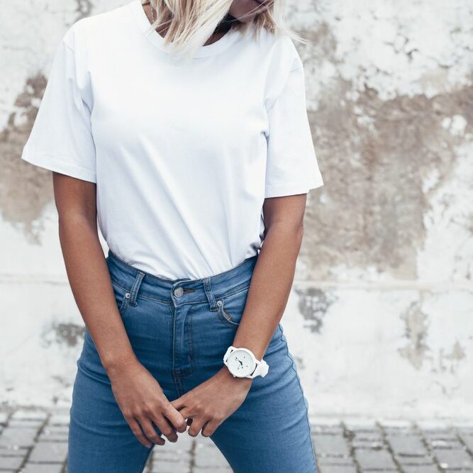 Hipster girl wearing blank white t-shirt and jeans posing against rough street wall, minimalist urban clothing style, mockup for tshirt print store